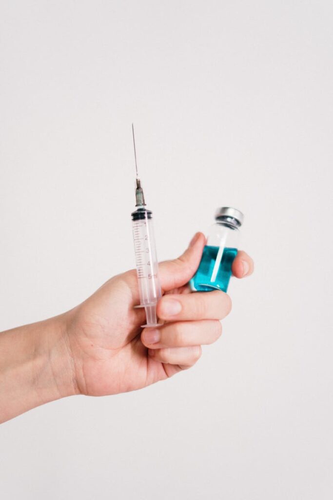 Close-up of a hand holding a syringe and a vaccine vial on a white background.