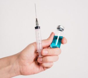 Close-up of a hand holding a syringe and a vaccine vial on a white background.
